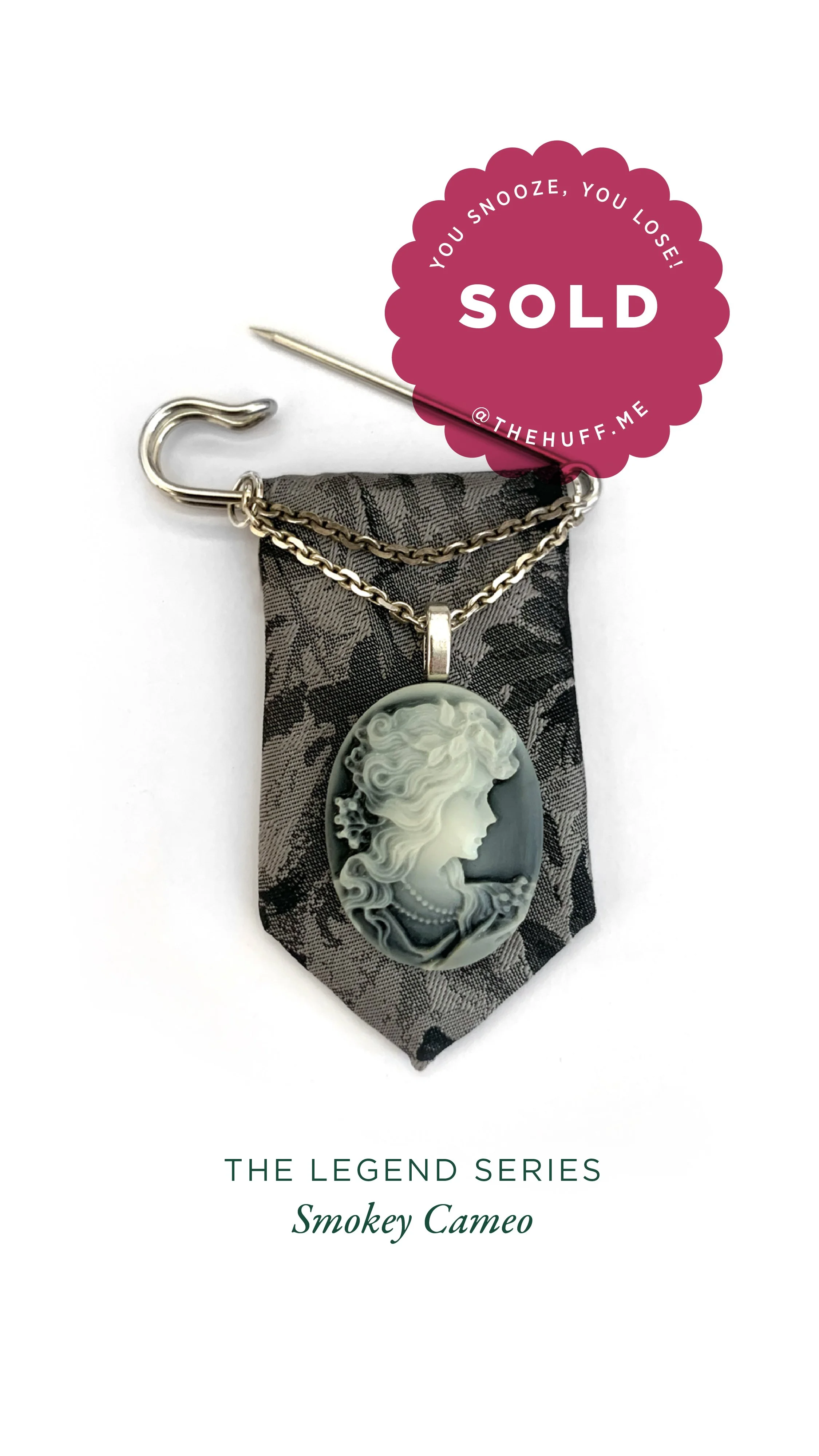 A cameo pendant with a profile of a woman's face, hanging by a chain, displayed on a black floral fabric background, with a sold notification sticker.