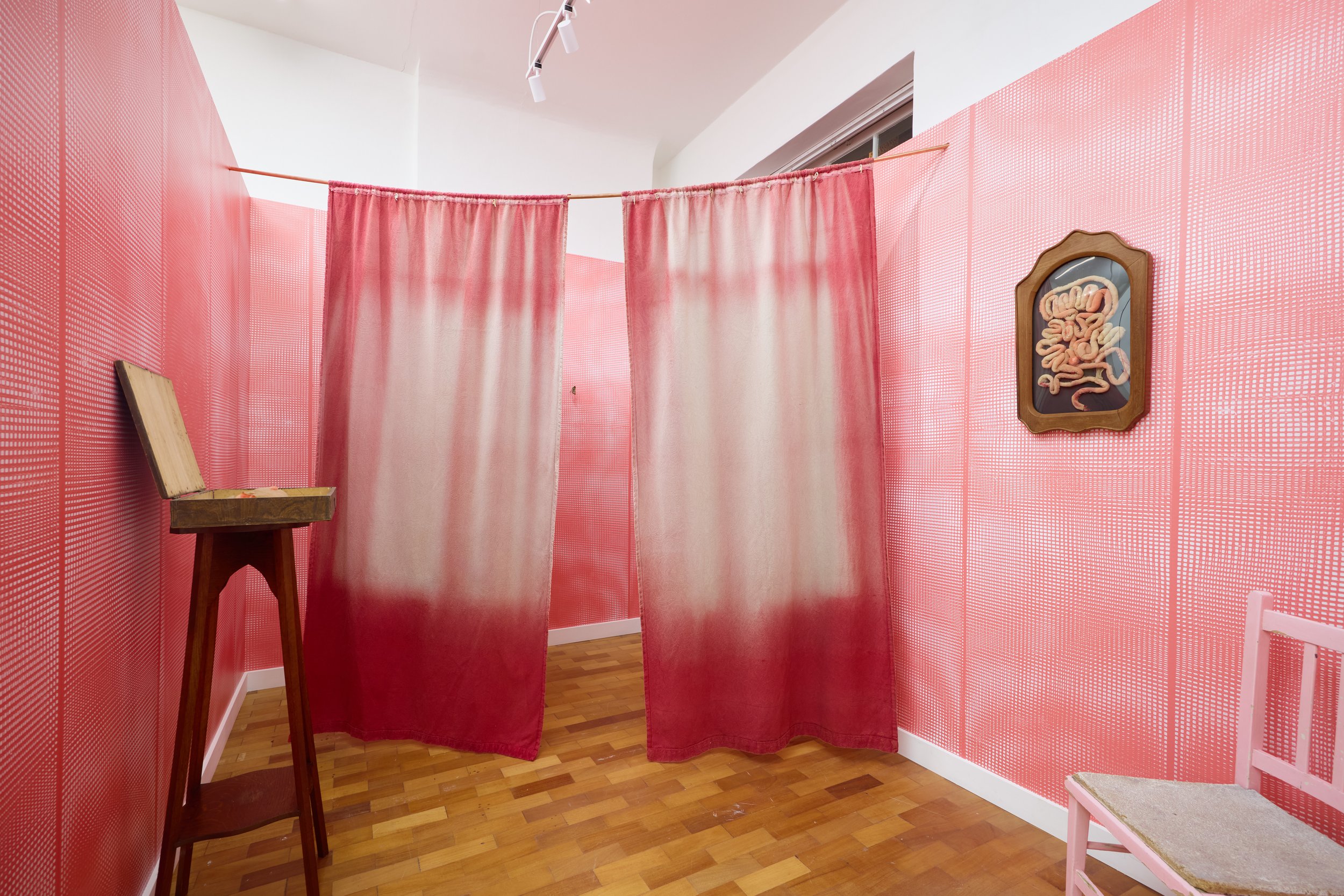 Echo Soho, an art installation with red curtains hanging from a rod in a room with red dotted wallpaper, a framed artwork featuring abstract shapes, a wooden stool, and a pink chair with a woven seat.