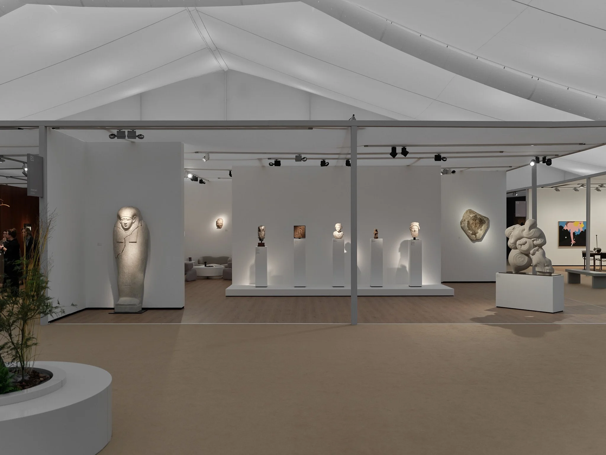 Interior of an art gallery, ArtAncient at Frieze London, with sculptures and a potted plant