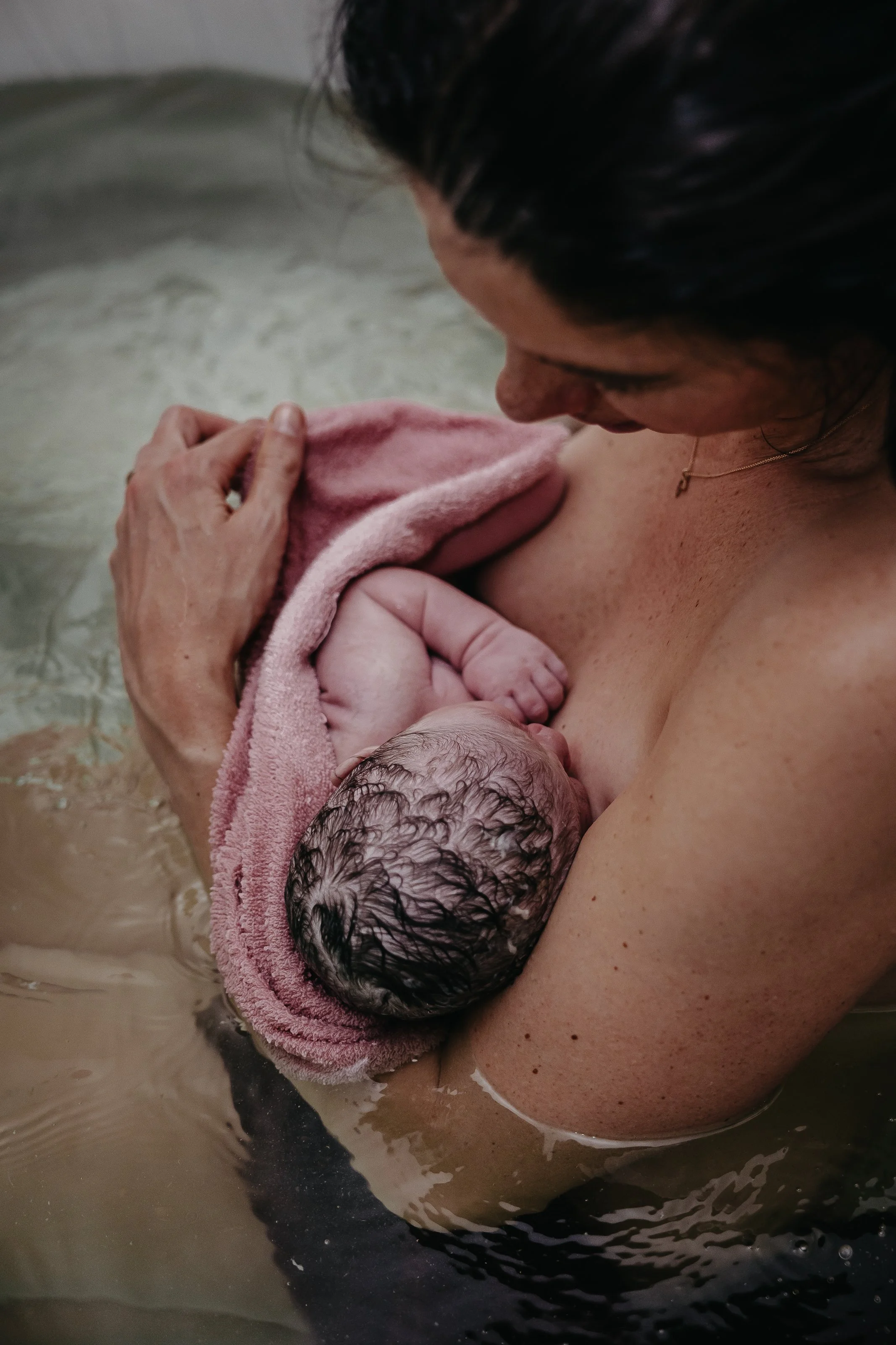 Dokumentarische Geburtsfotografie in Hannover - Mutter hält ihr neugeborenes Baby nach der Geburt im Wasser - Wassergeburt