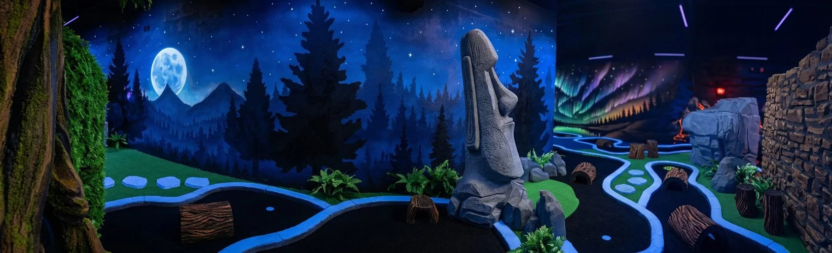 A vibrant, enchanting indoor blacklight miniature golf course designed by Charmed Playhouses. The fantastical setting features glowing 3D mushroom statues, a large gnarled tree, and elaborate stone structures. The walls are covered in striking, color