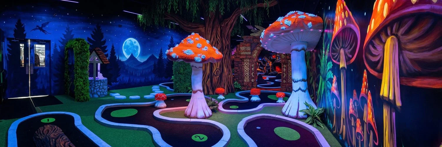 A vibrant, enchanting indoor blacklight miniature golf course designed by Charmed Playhouses. The fantastical setting features glowing 3D mushroom statues, a large gnarled tree, and elaborate stone structures. The walls are covered in striking, color