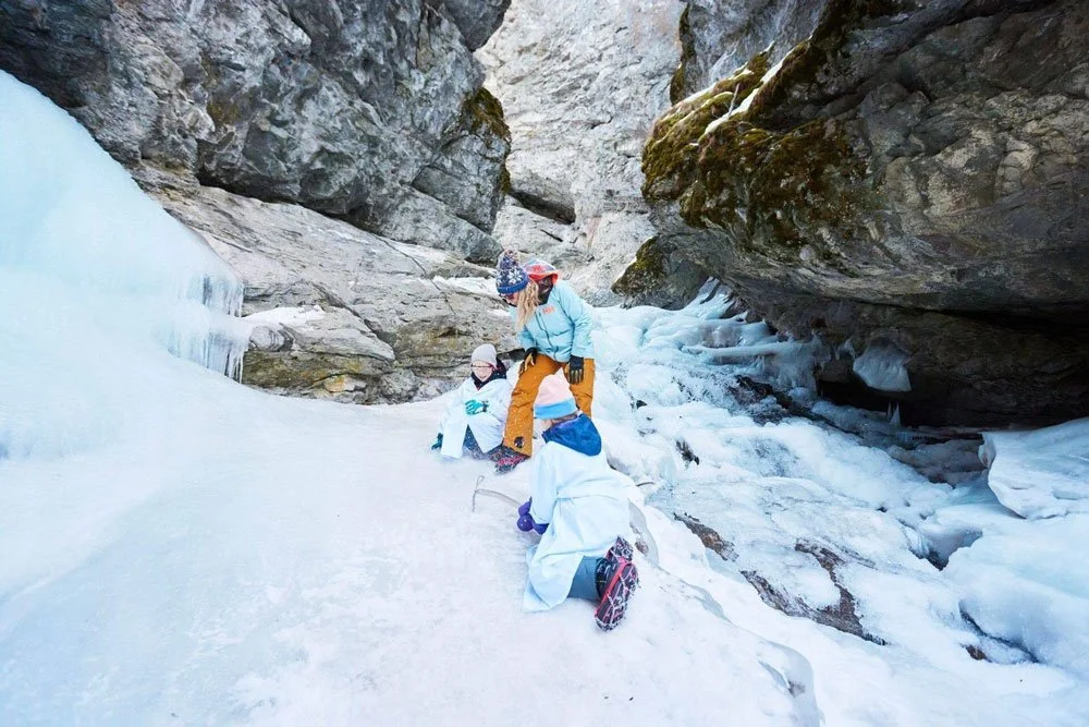 Group of people climbing icy terrain in a narrow canyon with rocks and ice formations.