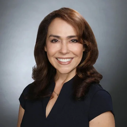 Close-up of a smiling woman with brown hair, wearing a black top against a gray background.