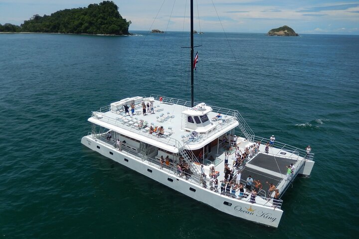 Large white yacht labeled 'Ocean King' anchored in a calm ocean with small islands in the background, people on deck enjoying the day.