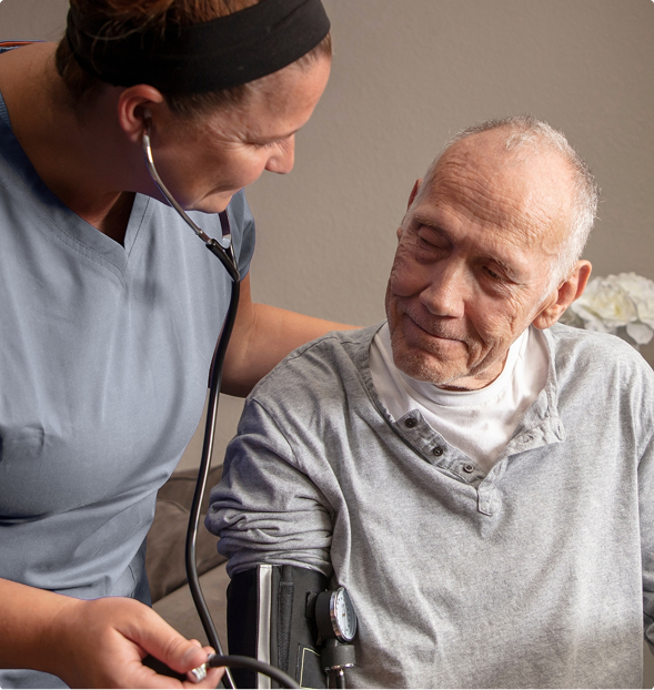 Nurse using a stethoscope to check an elderly man's heartbeat while providing compassionate hospice care at home.