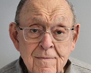 Close-up of an elderly man with glasses, furrowed brow, and neutral expression