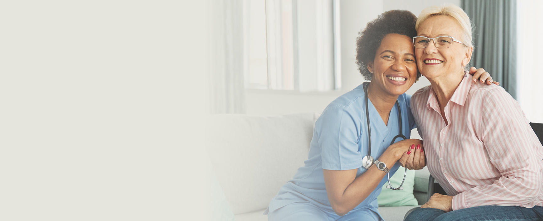 Hospice isn't an ending. It can ensure a better quality of life at the end of life. A healthcare professional in blue scrubs and a stethoscope embraces an elderly woman with glasses, both smiling happily in a bright room.