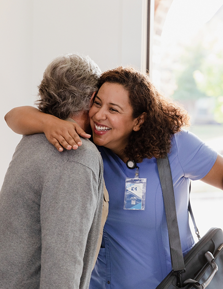 A nurse in blue scrubs hugging an older woman at a healthcare facility