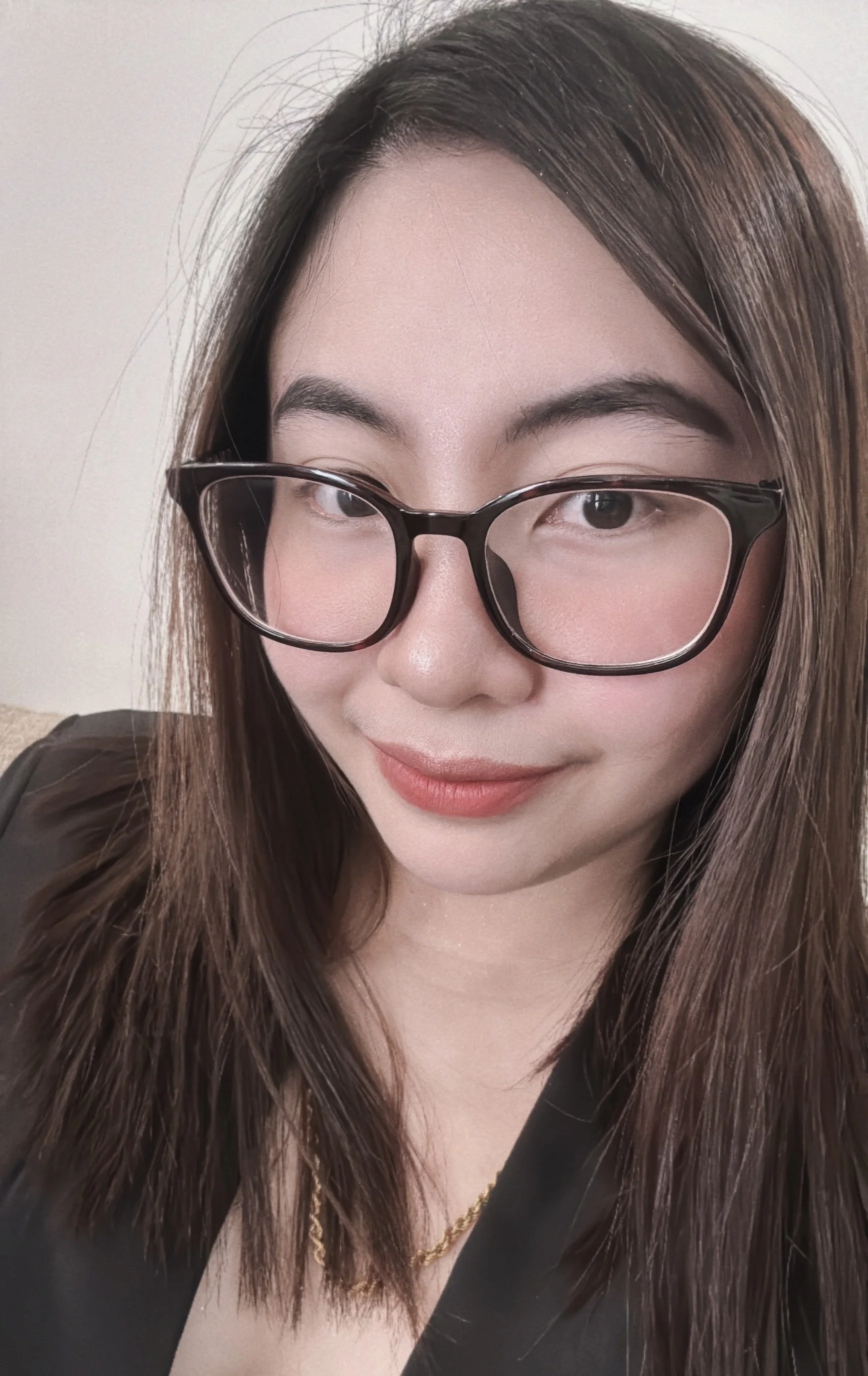 A young woman with shoulder-length dark hair smiling outdoors with a background of greenery and blooming flowers