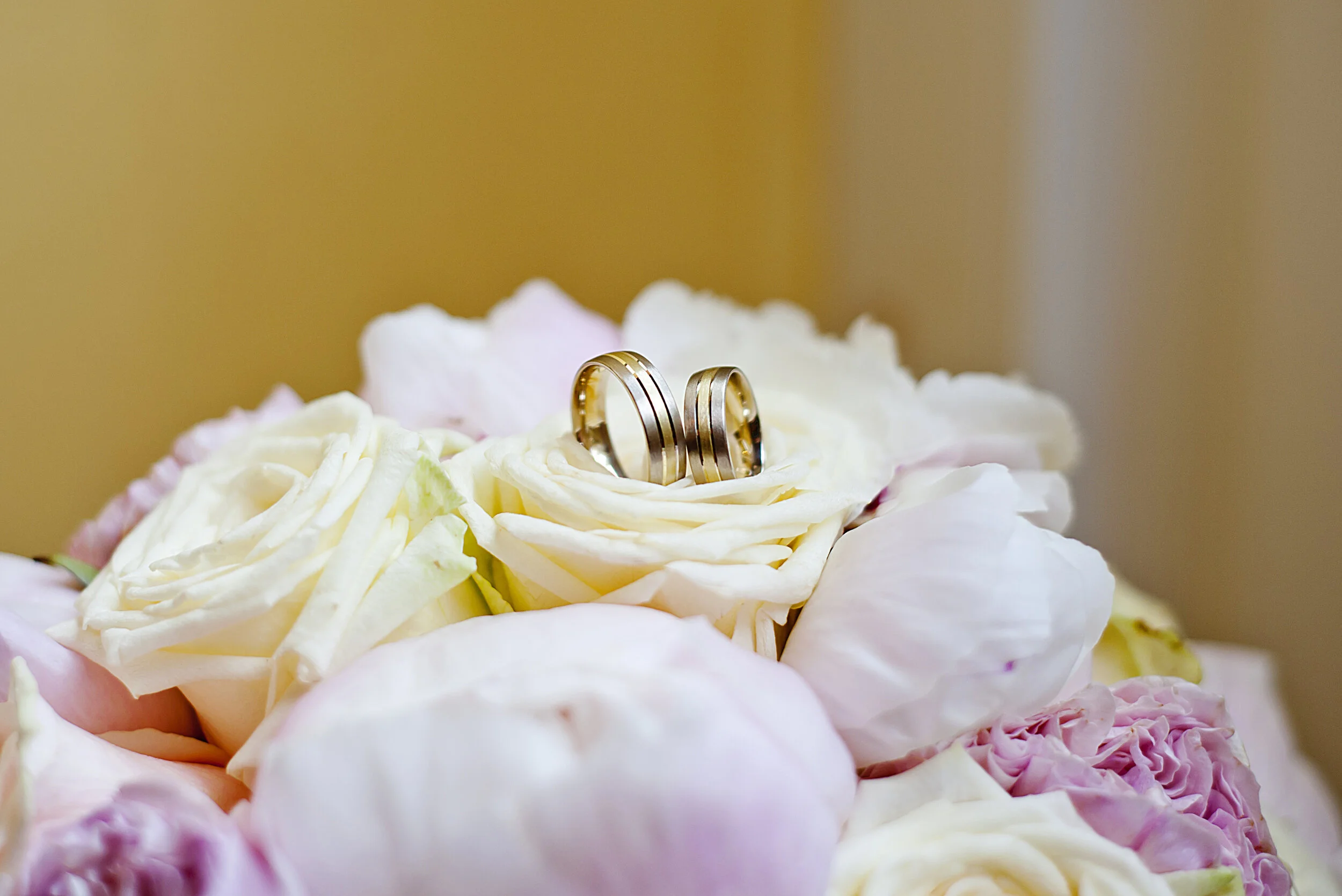 Close-up of wedding rings on a bouquet of white and pink roses.