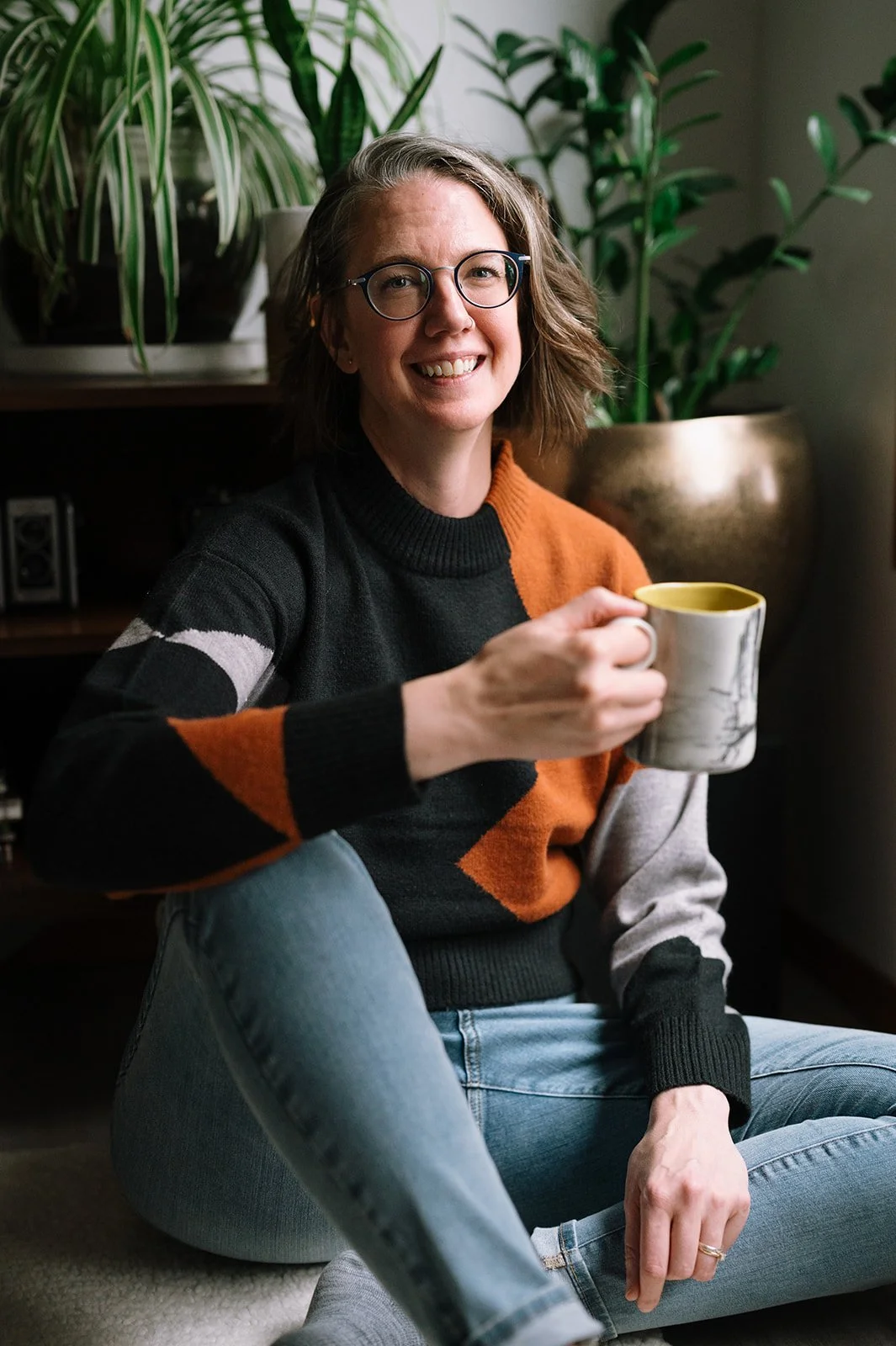 Hilary sitting in front of some plants, holding a mug and smiling.