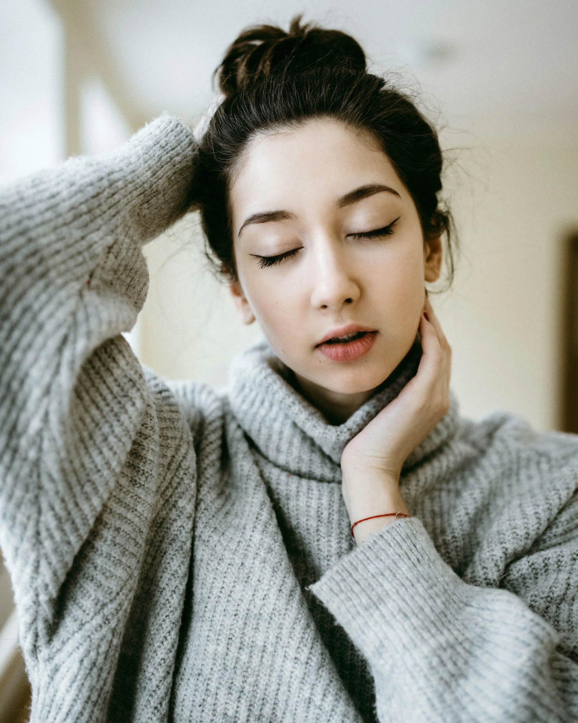 a woman looking tired or in pain, with her hands on her head and neck as if to massage them