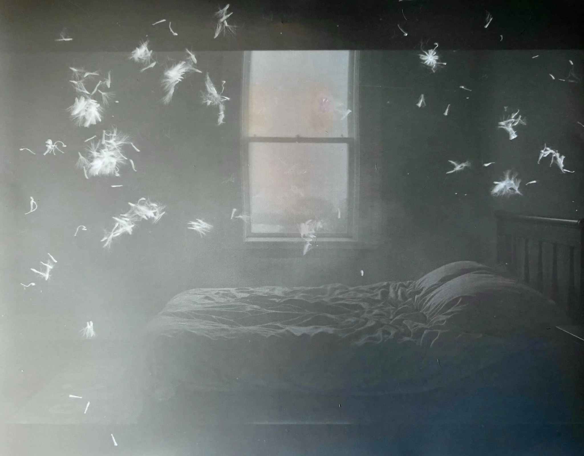 Une chambre sombre avec un lit en désordre et une fenêtre laissant entrer peu de lumière. Des peluches ou plumes blanches flottent dans l'air.