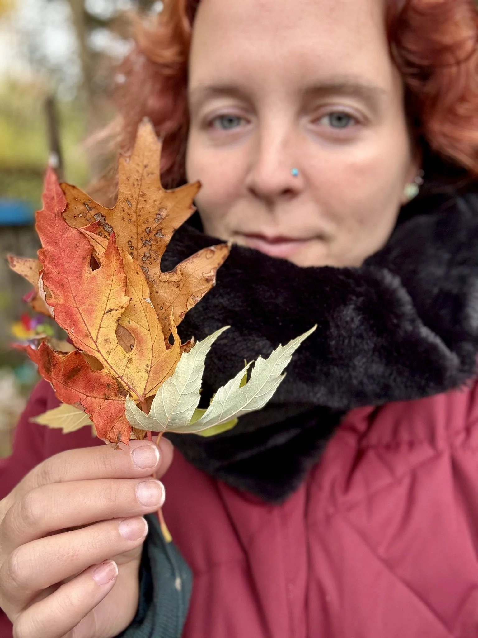 Une femme avec des cheveux roux tient un bouquet de feuilles d'automne en pleine nature.