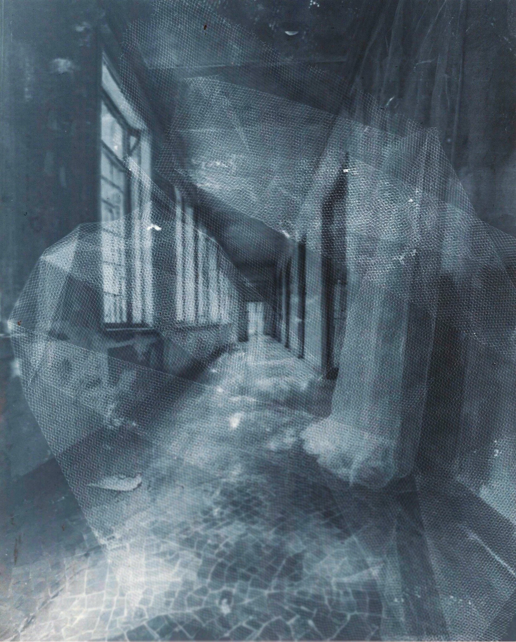 Intérieur d'un bâtiment abandonné avec fenêtres, murs dégradés et débris au sol, vue à travers un filet ou une grille.