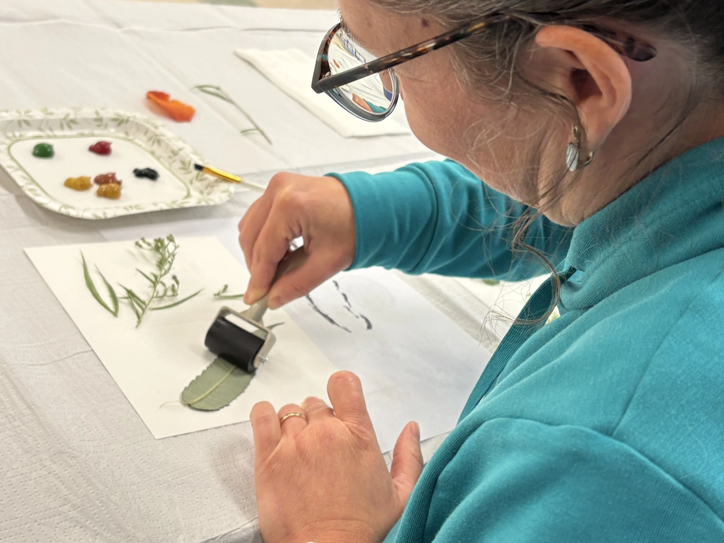 Une femme faisant de l'art botannique, utilisant un rouleau encreur pour appliquer de l'encre noire sur des feuilles et des plantes sèches.