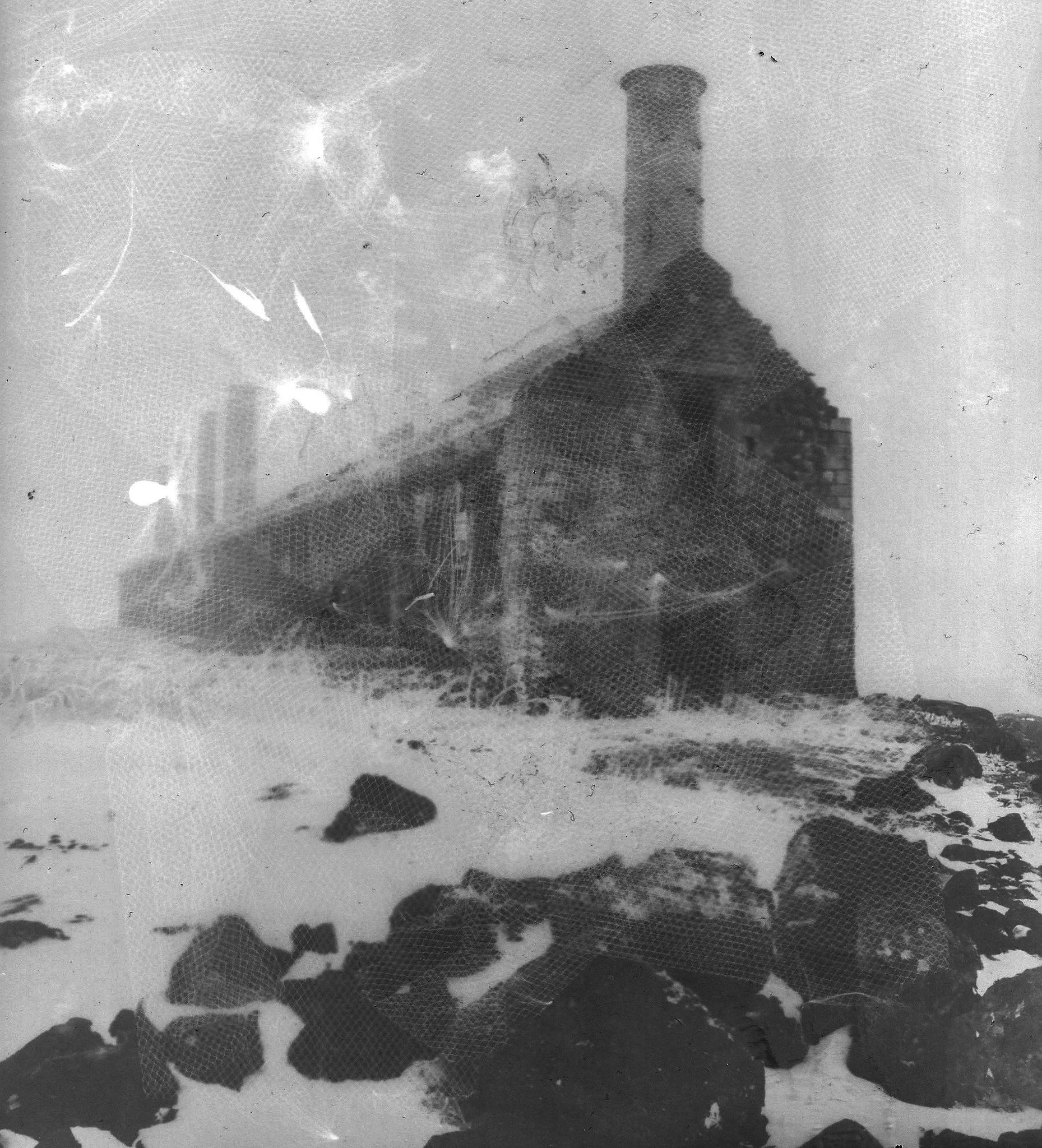 Une vieille photo en noir et blanc d'une maison en pierre avec une cheminée, entourée de rochers et enneigée.