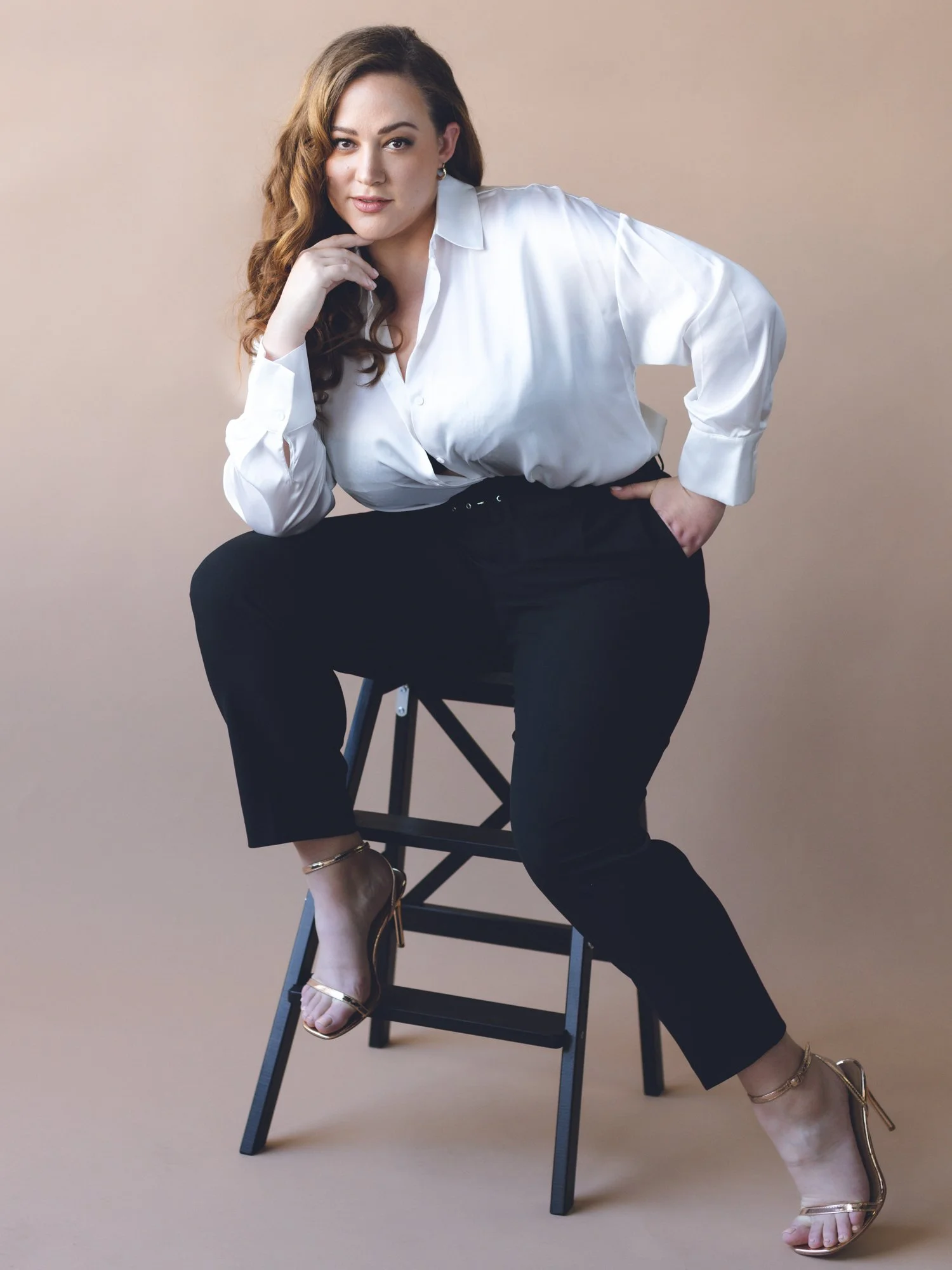 Woman sitting on a stool with a white shirt on and black pants.