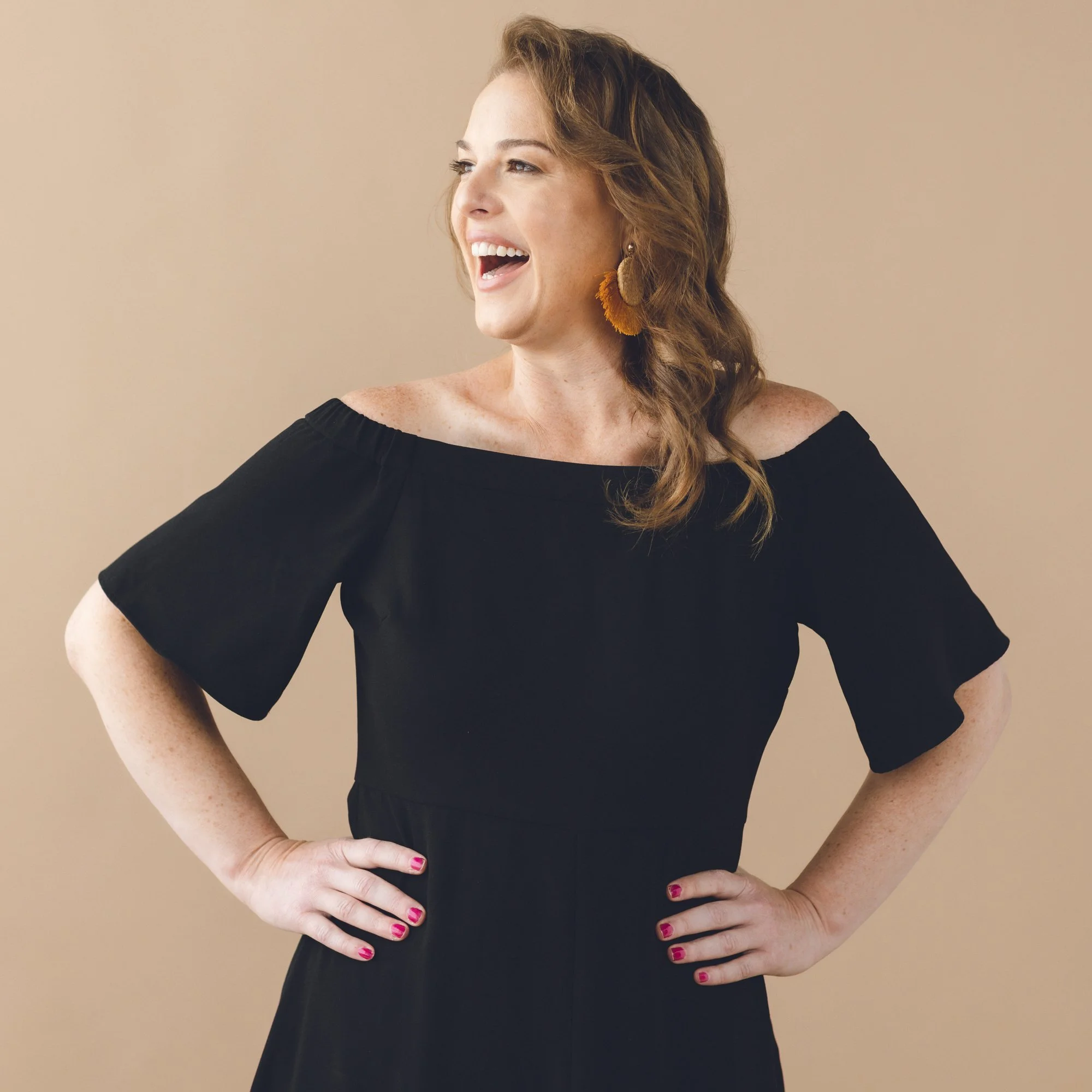 Woman smiling with a black dress on and a cream background. 
