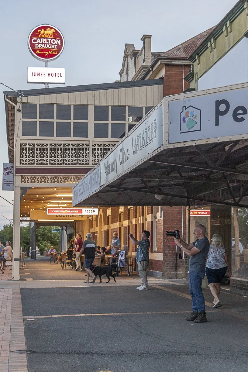 Locals and visitors to the Junee Hotel have cameras pointed towards a train at the level crossing. Scott Gould A Railway Life