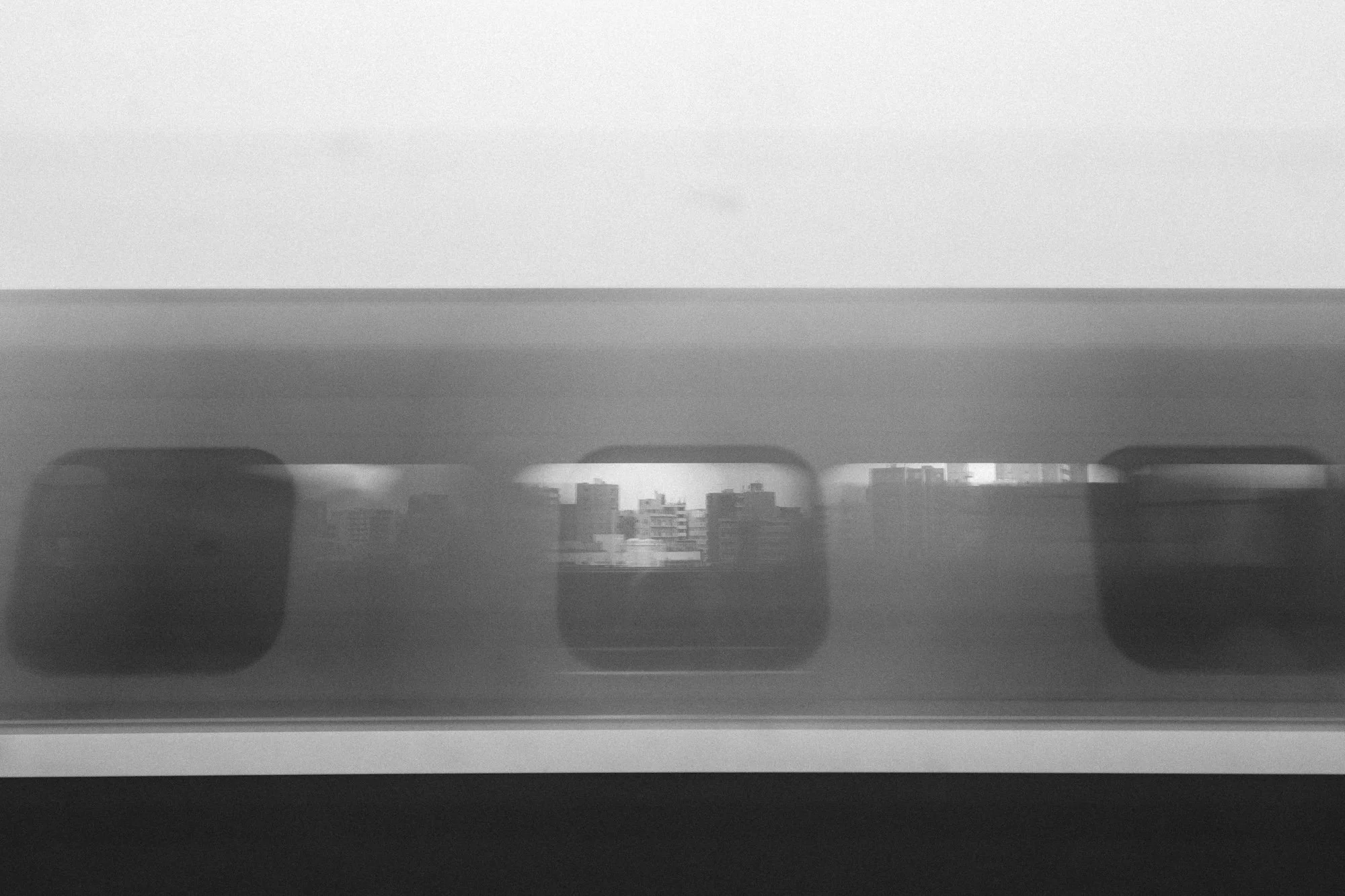 A Railway Life black and white photo taken while travelling north to Kumagaya on the outskirts of Tokyo from one Shinkansen of, and through a Tokyo bound train.