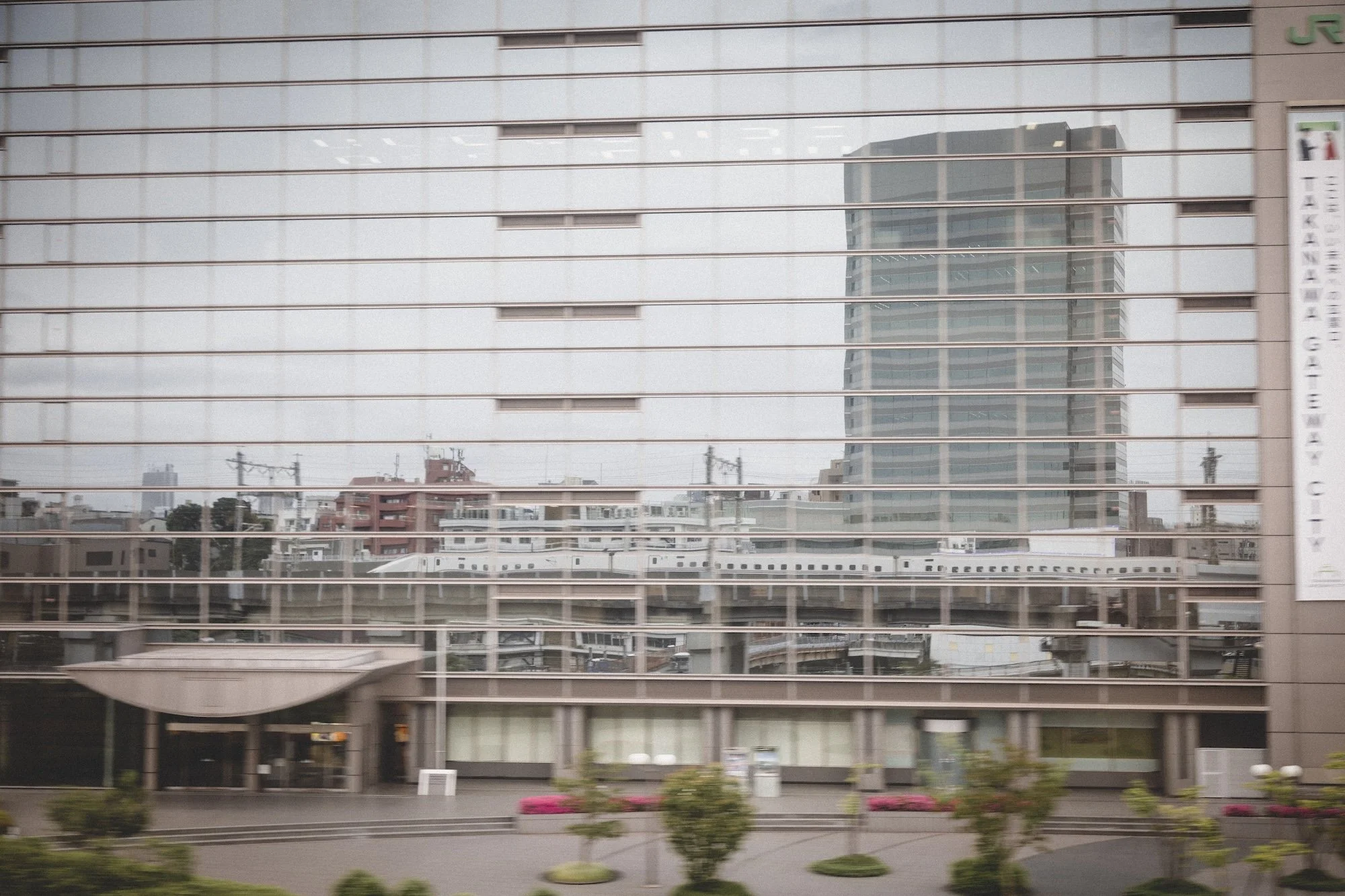 Scott Gould A RailwayLife photography an Osaka bound Shinkansen is reflected in the JR office building at Takanawa Gateway city.