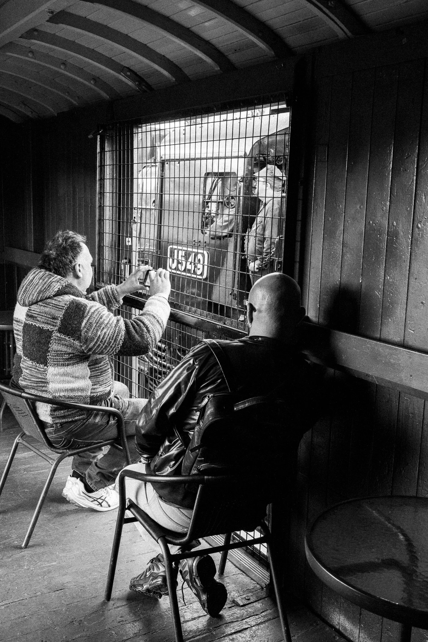 Two people aboard the Steamrail Victoria Vintage Train from Castlemaine watch as the Victorian Goldfields Railway locomotive J 549 runs beside them. Black and white 22 August 2026 Scott Gould A Railway life