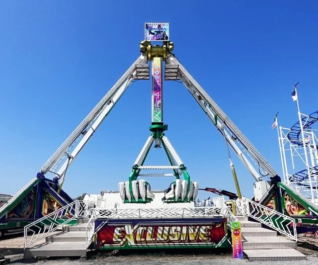 Grande roue d'attraction avec une structure colorée et le panneau "Exclusive" au premier plan, sous un ciel clair.