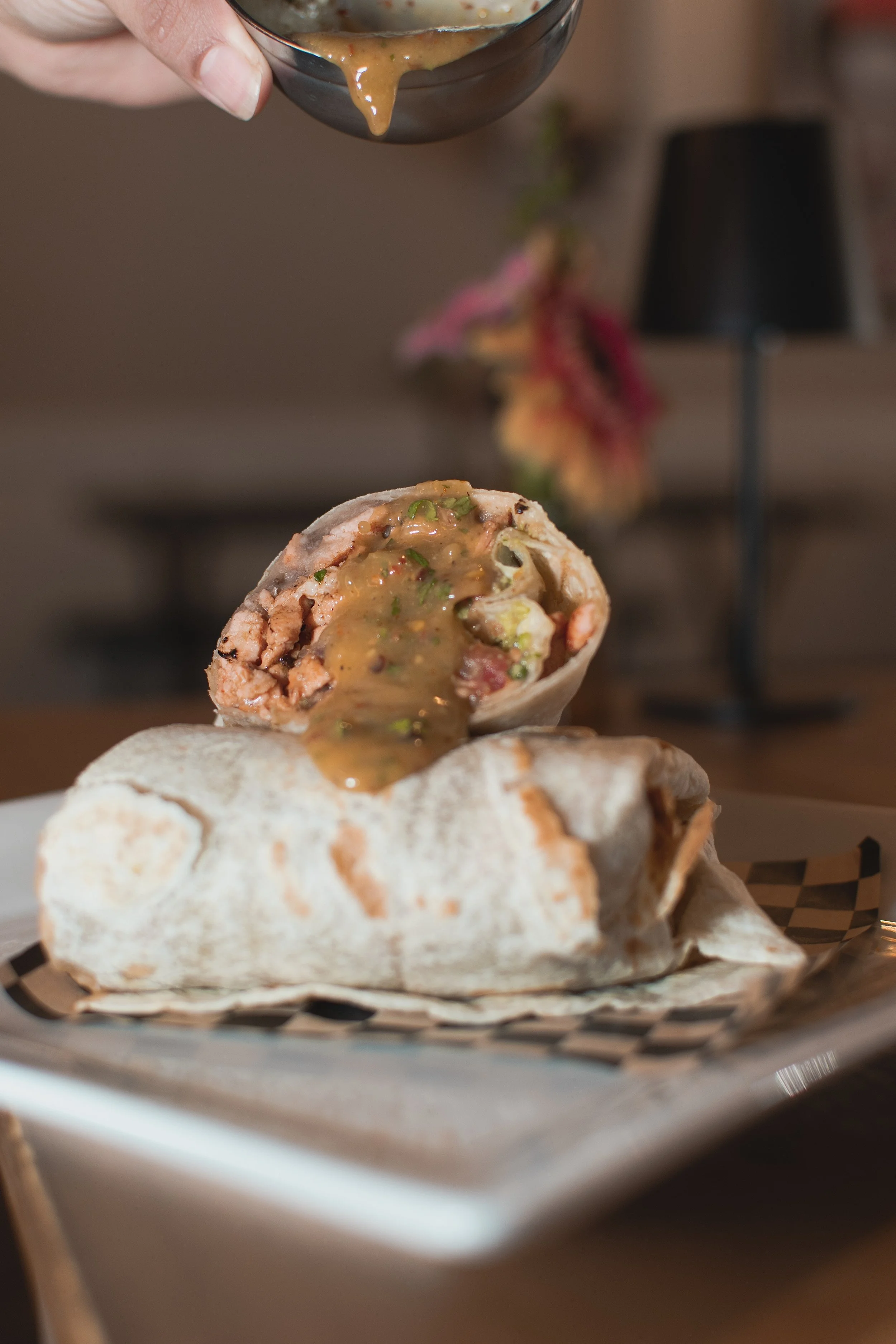 A burrito wrapped in a white flour tortilla, cut in half to reveal filling of meat, vegetables, and sauce, placed on a basket lined with parchment paper with a second burrito underneath.