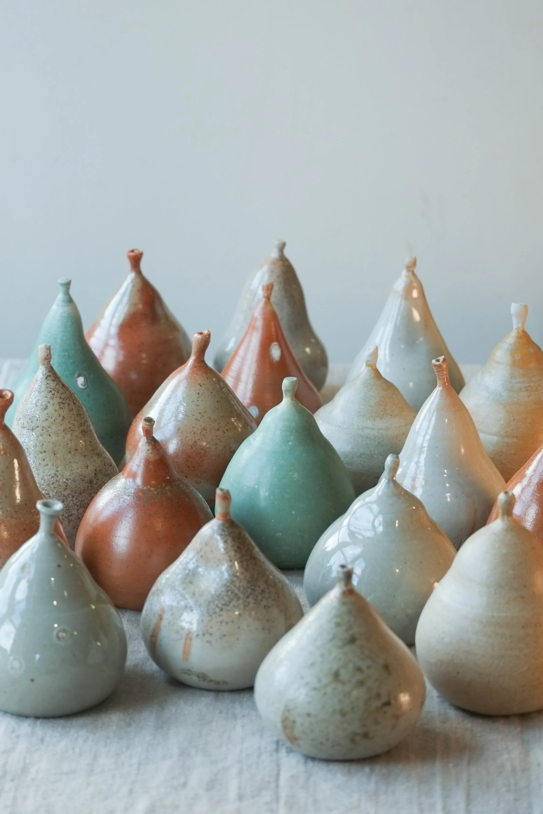 A collection of glazed ceramic pears in various pastel colors, arranged on a white surface.