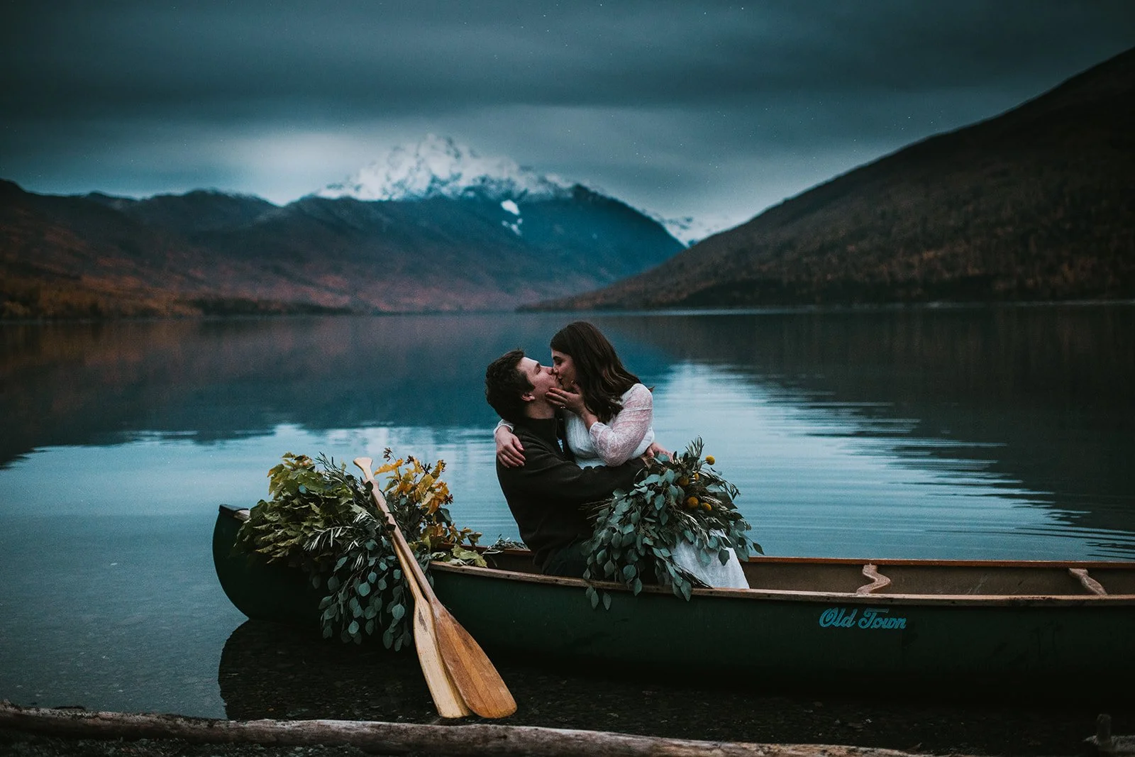 A couple in a boat on a lake, sharing an intimate moment with mountain scenery in the background.
