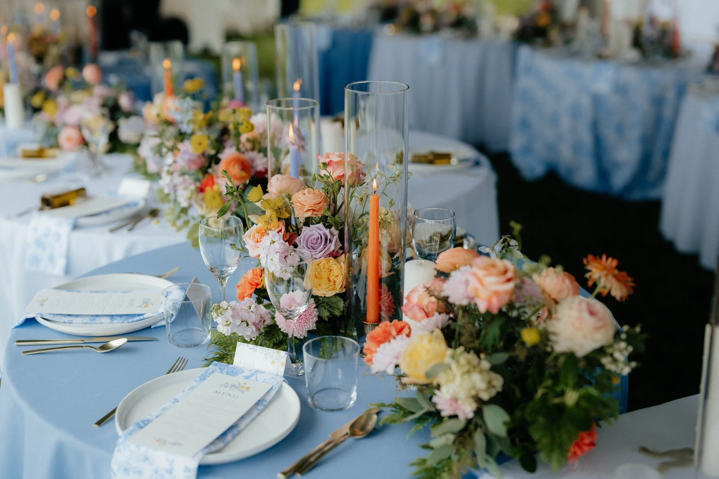 Elegant dining table with pastel-colored flowers, candles, and glassware for a formal event.