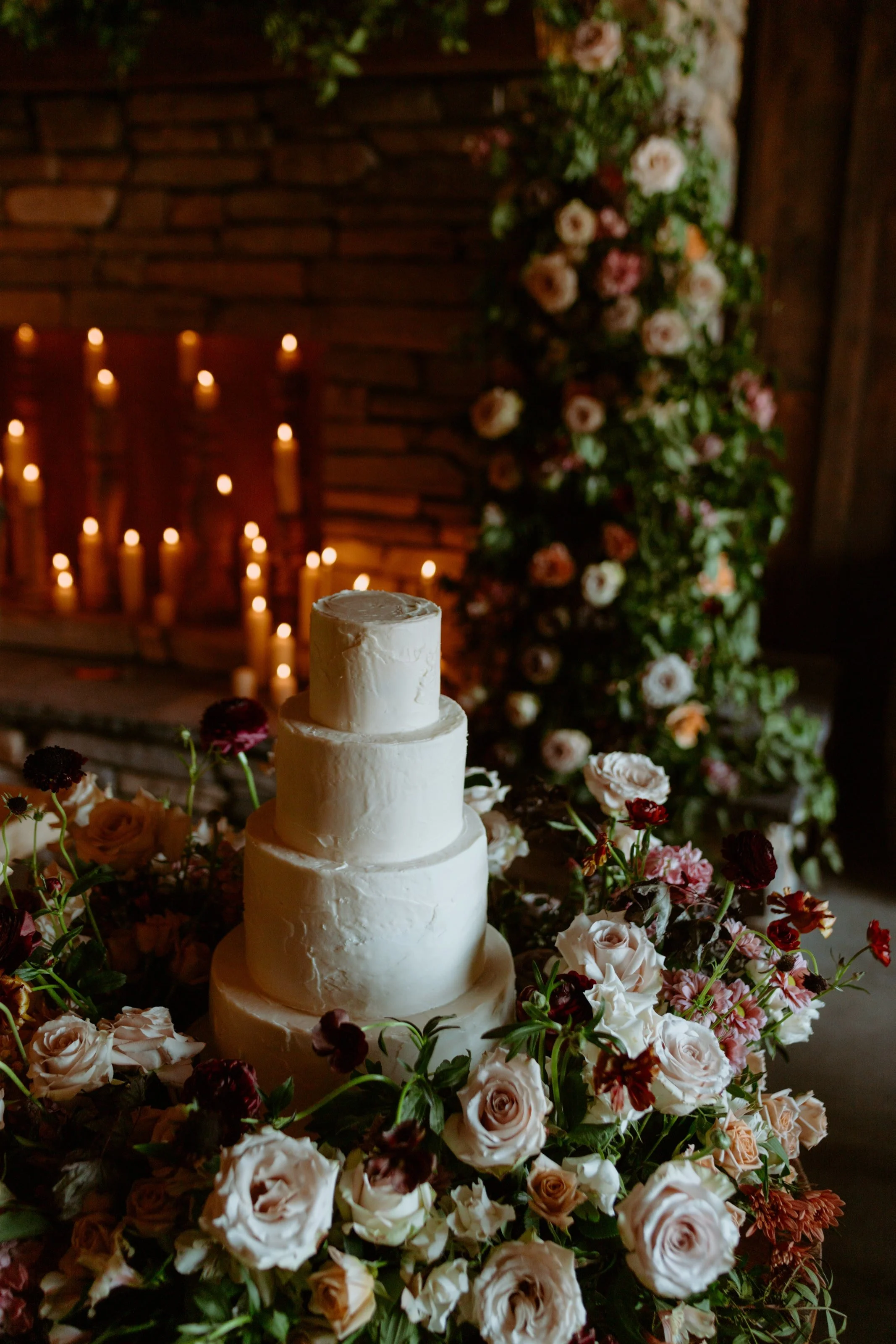 Three-tiered white wedding cake surrounded by pink and white roses and various flowers.