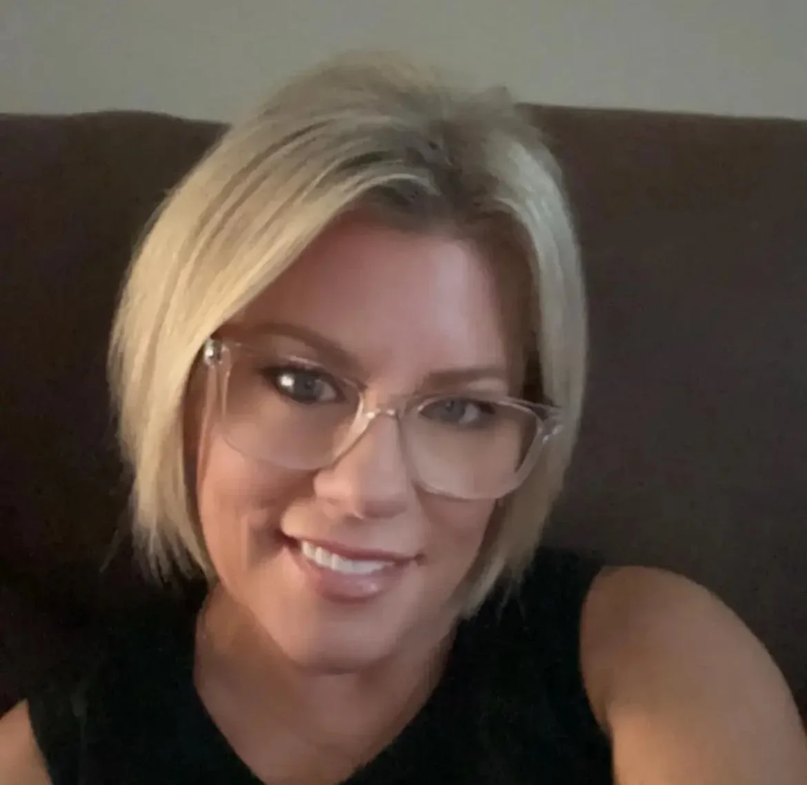 A woman with blonde hair, glasses, and a black sleeveless top smiling at the camera.