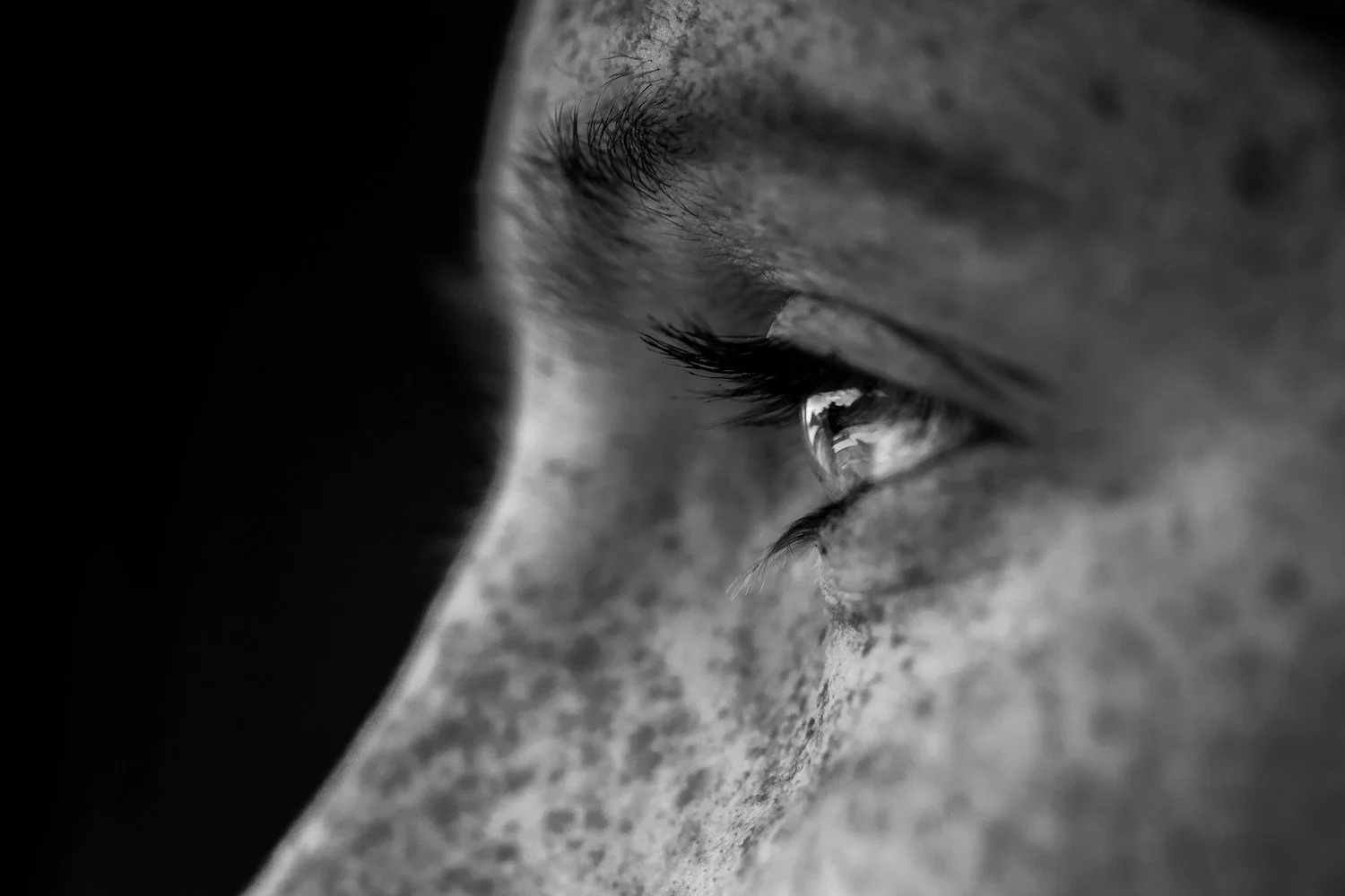 Close-up of a person's eye in black and white, showing detailed eyelashes and a reflection in the eye.