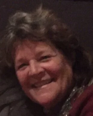 Smiling woman with short, curly hair wearing a dark top and a maroon jacket.