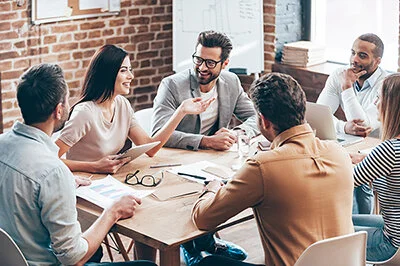 Group of six diverse professionals engaged in a meeting around a wooden table in a modern office.
