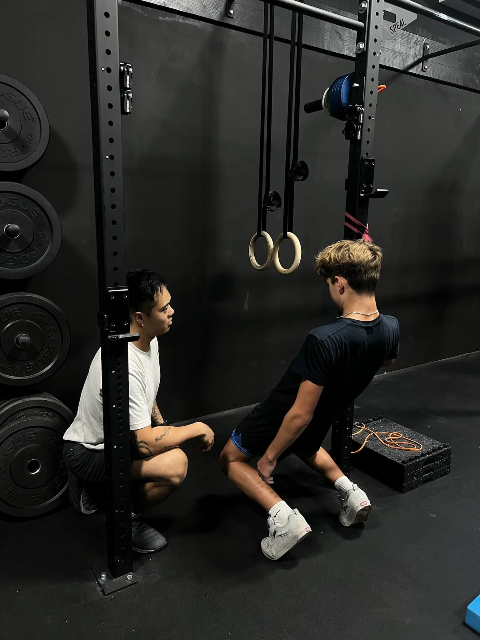 A young male cross-country athlete performing sissy squats for his knee pain with his physical therapist watching closely.