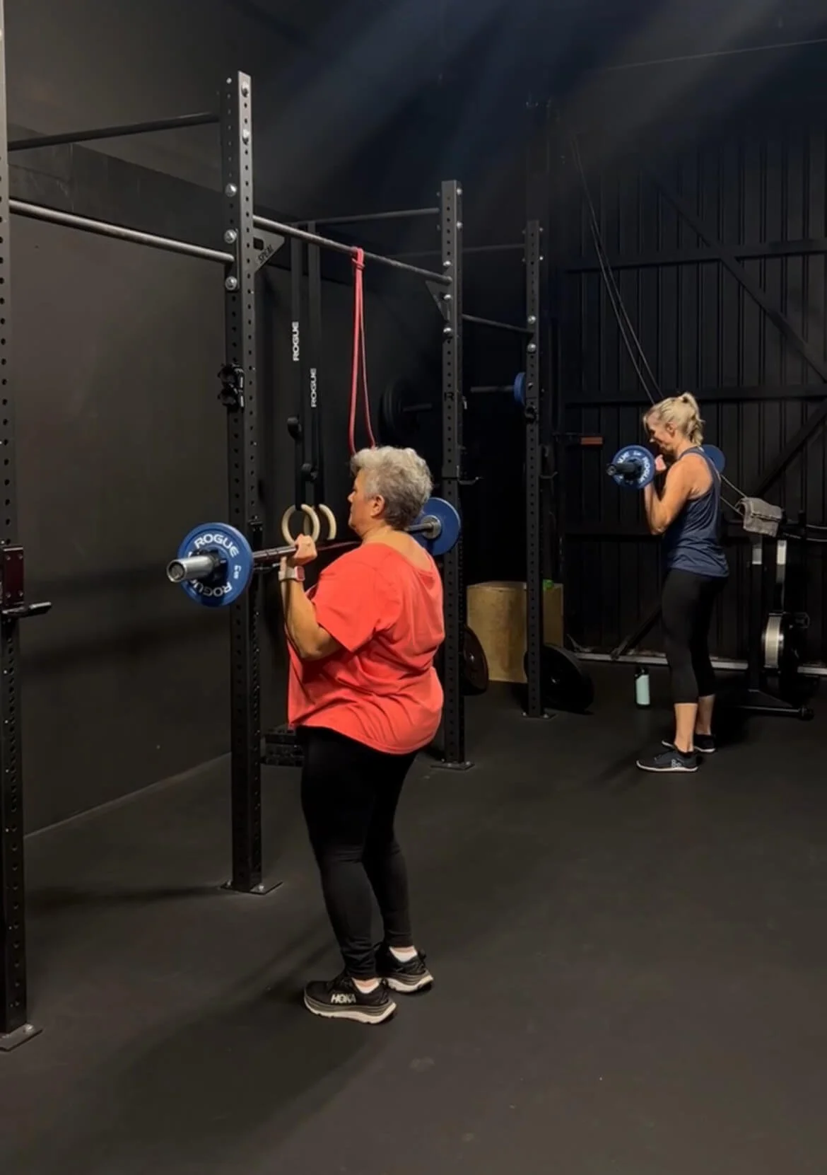 Two ladies performing barbell strict presses during a group physical therapy session.