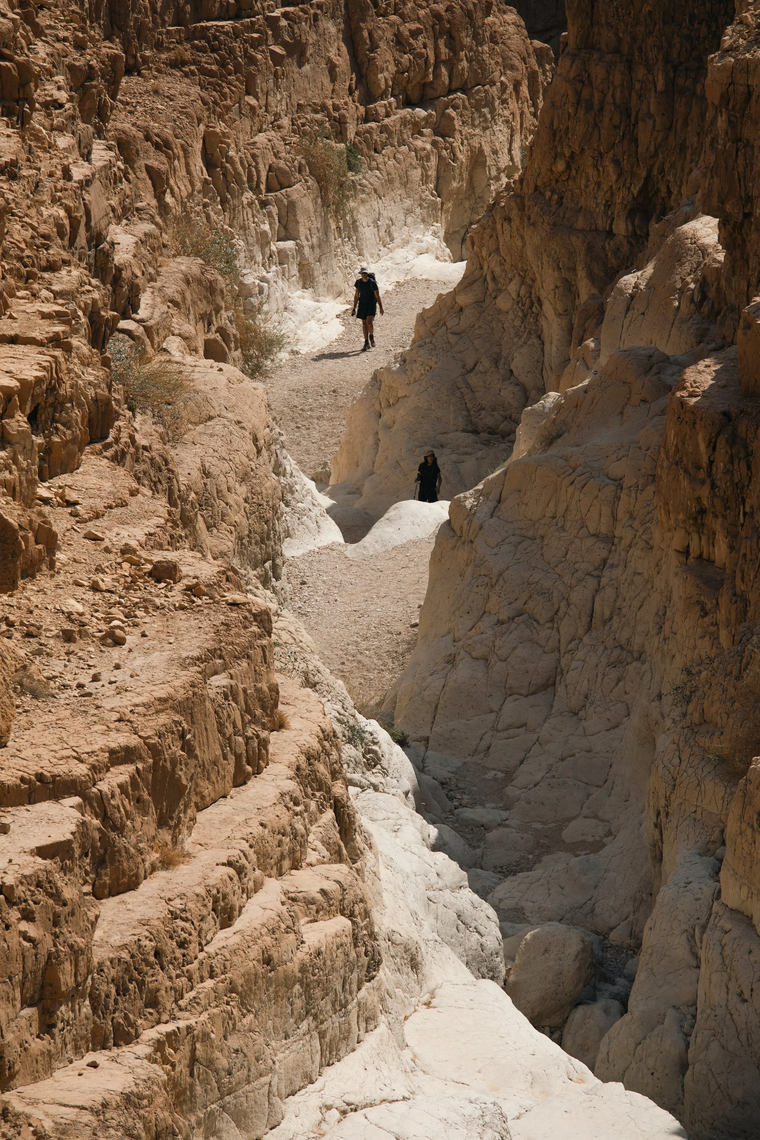 Hikers walking through a narrow rocky canyon with steep walls.