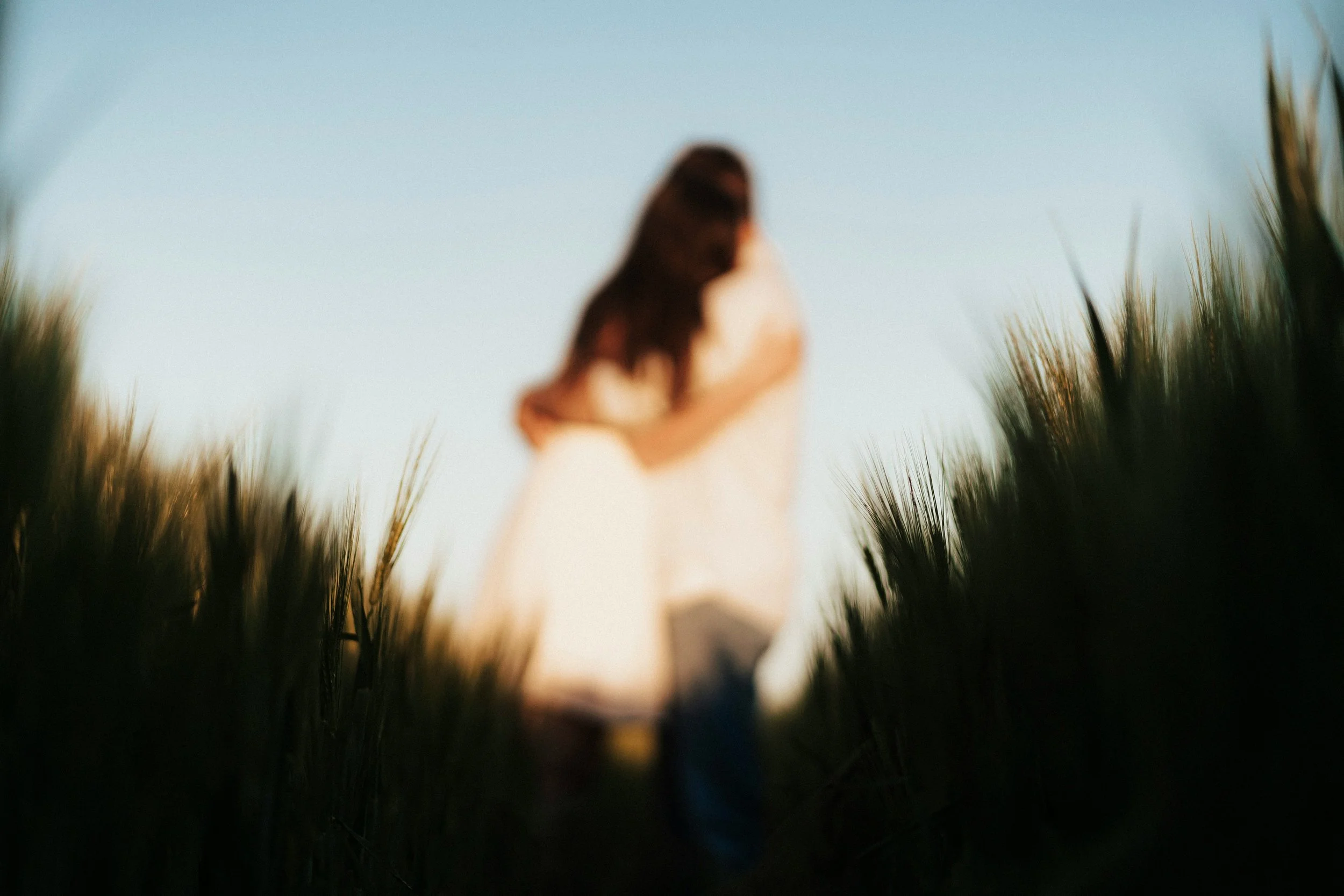 Blurry couple embracing in a field of tall grass under a blue sky.