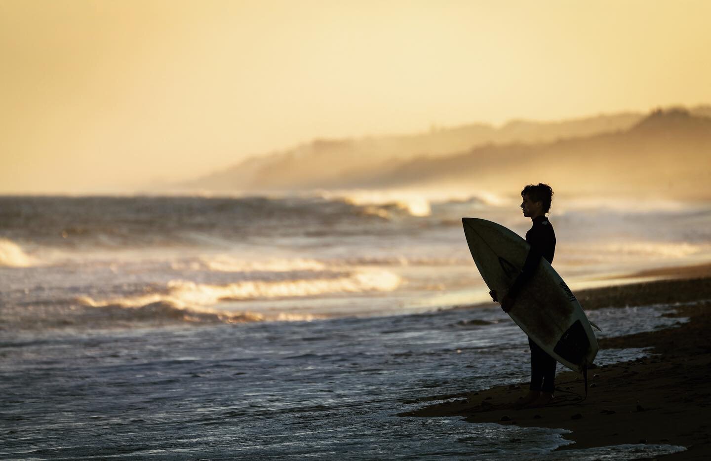 A boy studies the pattern of the waves before entering the water. It was late afternoon by the time I arrived at the beach and saw this figure. I waited for some other surfers and beach goers to exit the frame, and then took this shot. Backlit by gol