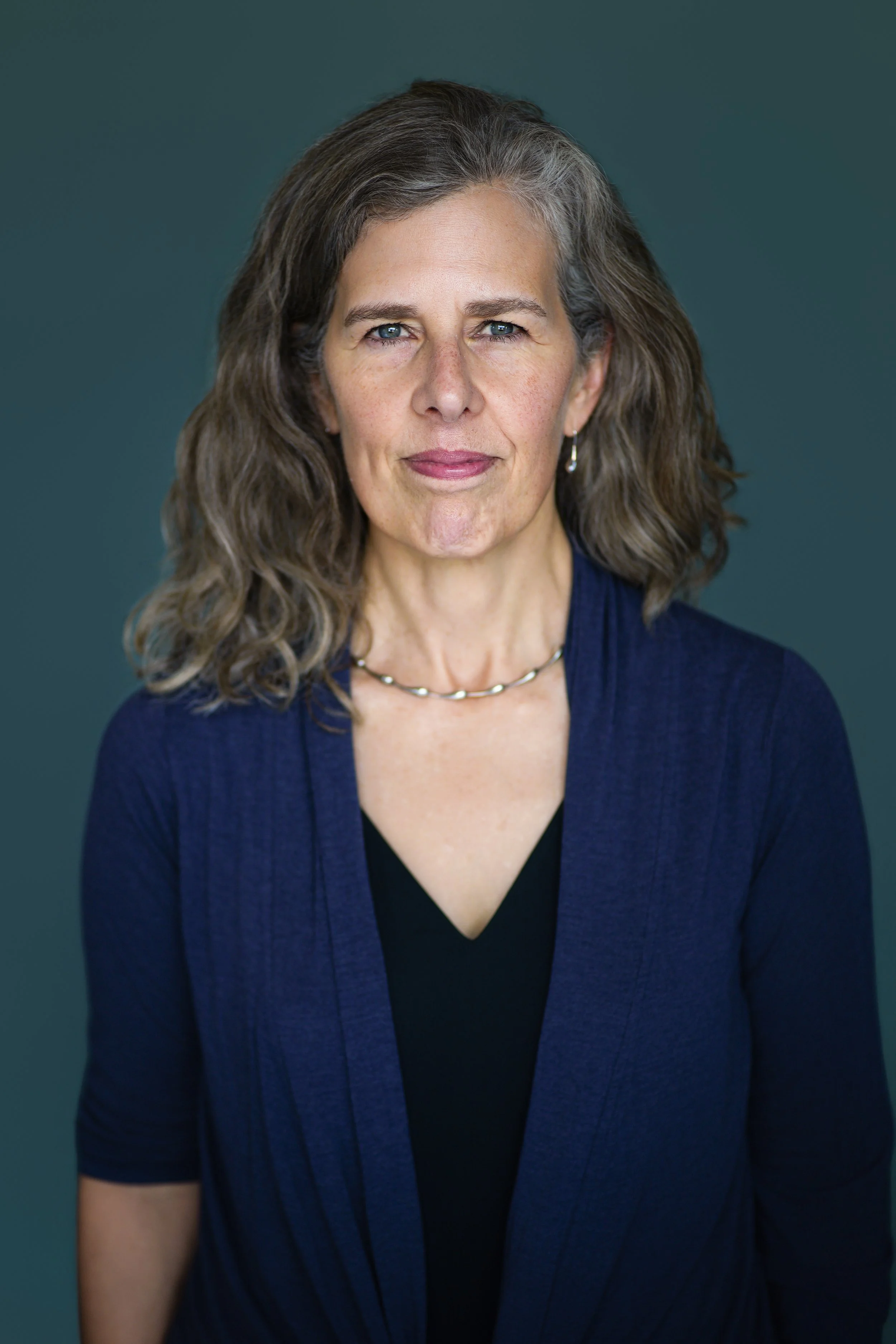 50-something woman with brown and greying hair looks into the camera with a slight smile
