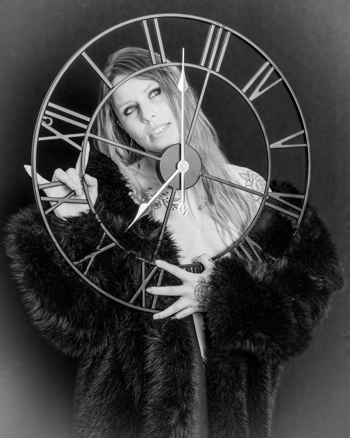 A woman with tattoos on her hand and chest, wearing a fur coat, holding a clock in front of her face, with overlapping clock's face showing Roman numerals.