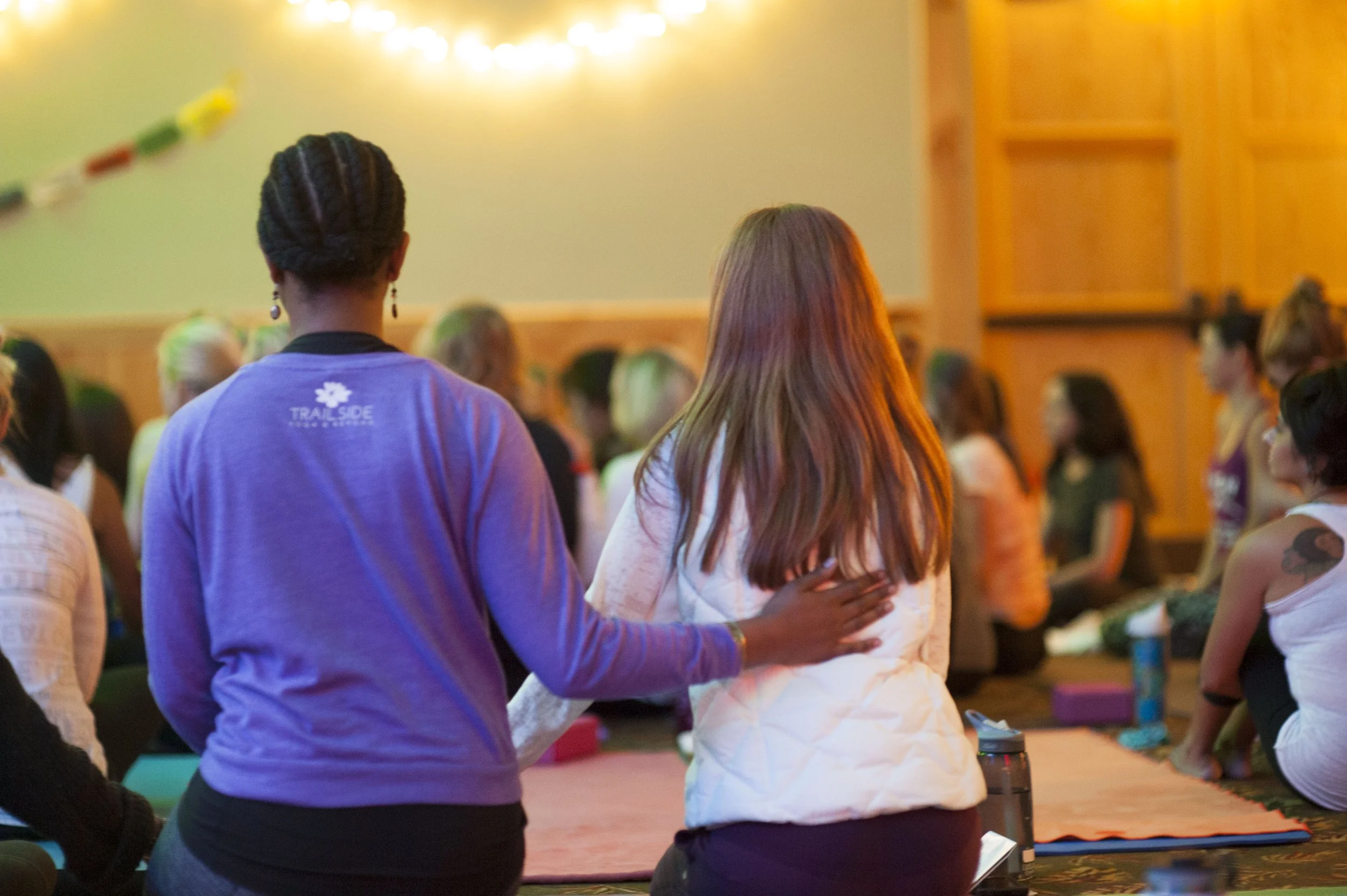 People gathered in a room, standing close together with one person resting a hand on another's shoulder, participating in a group activity or prayer.
