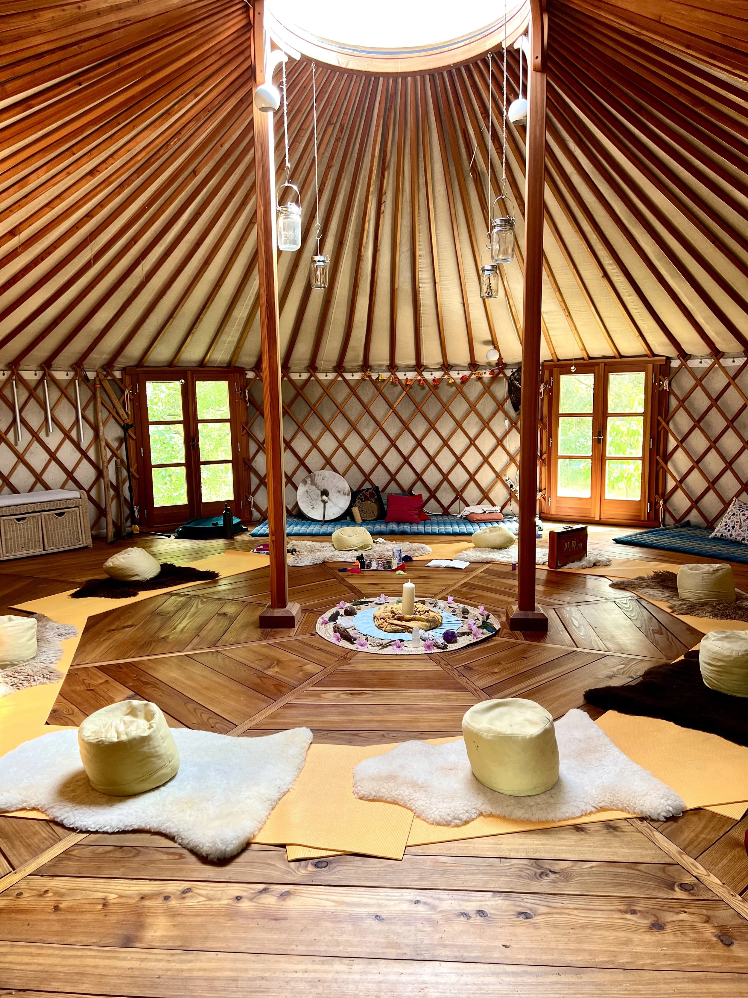 Innenraum eines Zelt mit Sitzkissen, Decke, Kerzen, Musikinstrumenten und Fenstern, Natur sichtbar außerhalb.