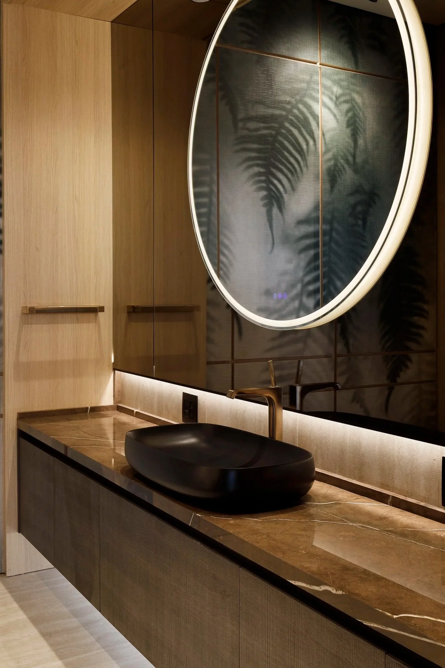 Detalle de lavabo negro sobre encimera veteada, con grifo dorado y espejo circular iluminado.