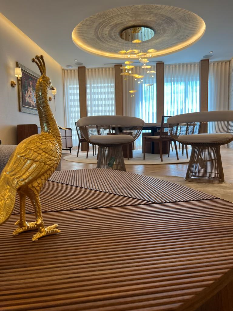 Escultura dorada de ave junto a una sala con mobiliario contemporáneo y ventanales.