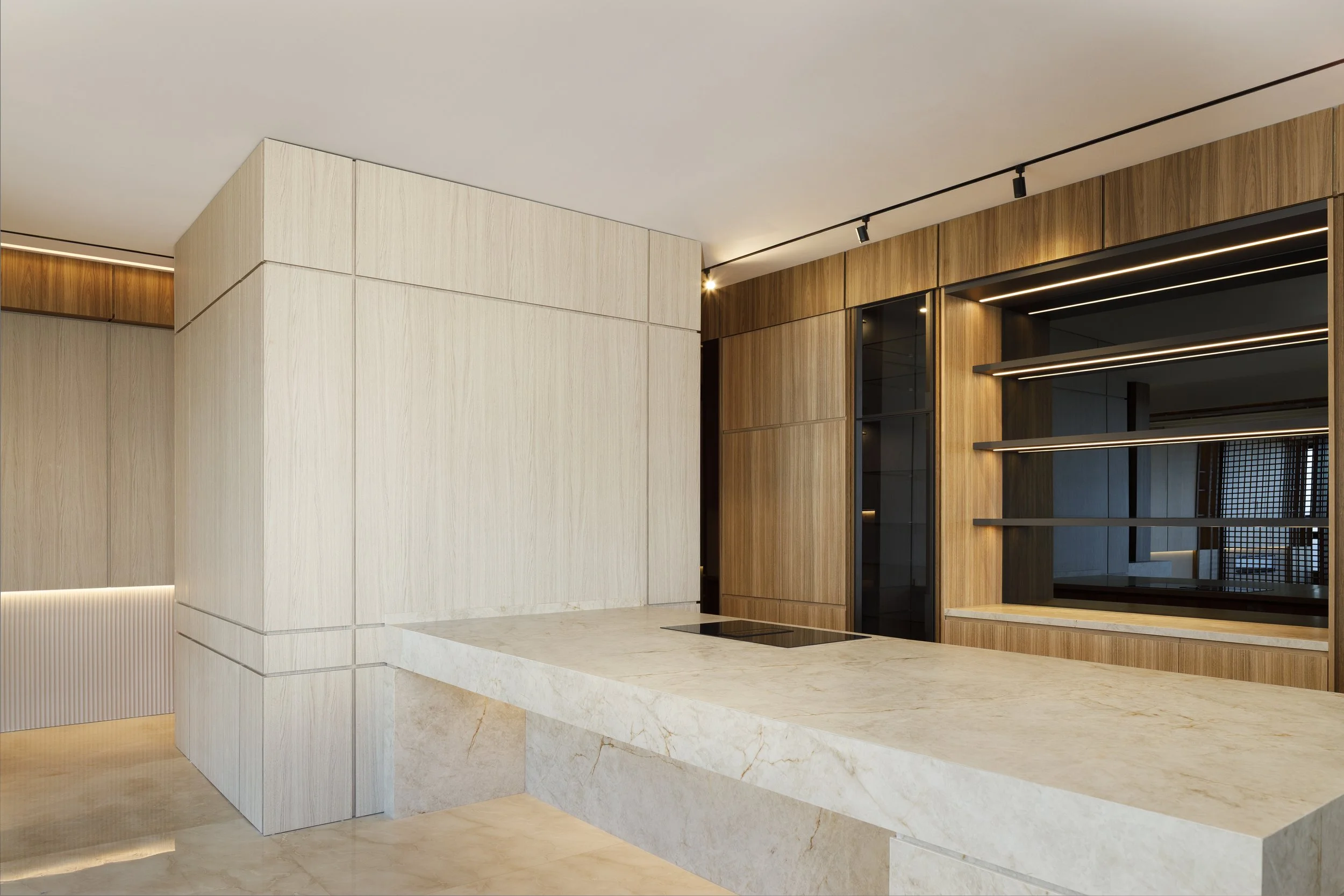 Interior moderno de una cocina con superficies de mármol, paredes de madera y estanterías negras con iluminación incorporada.